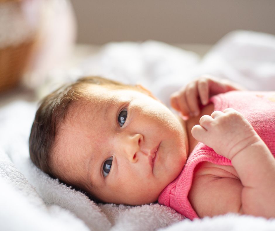 newborn baby laying down on back and looking directly into camera