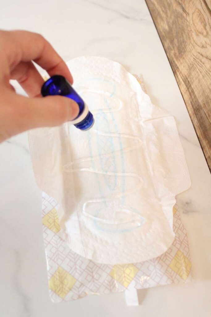 a picture of a maxi pad opened up with a hand holding a bottle of essential oils, applying it directly to the opened pad.
