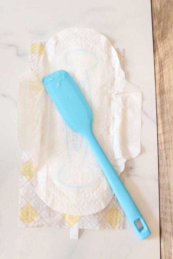 a picture of a maxi pad opened up with a small blue spatula laying on top of it.