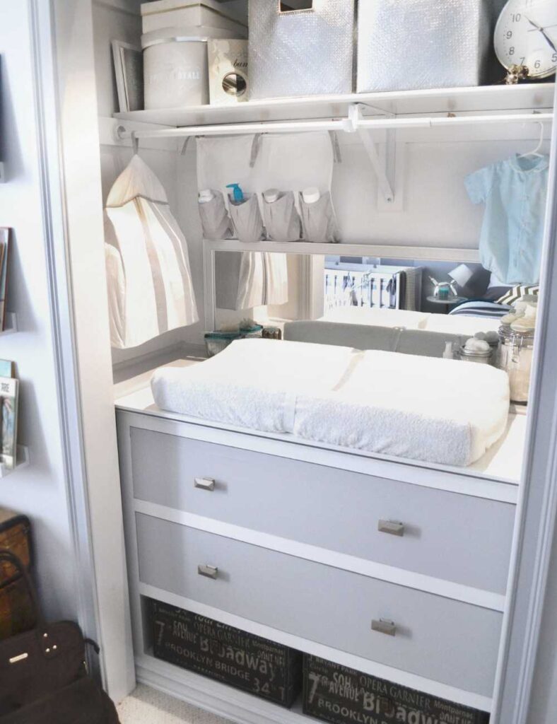 picture of a nursery closet with a dresser and changing table inside of it, and a clothing rod at the top with additional storage