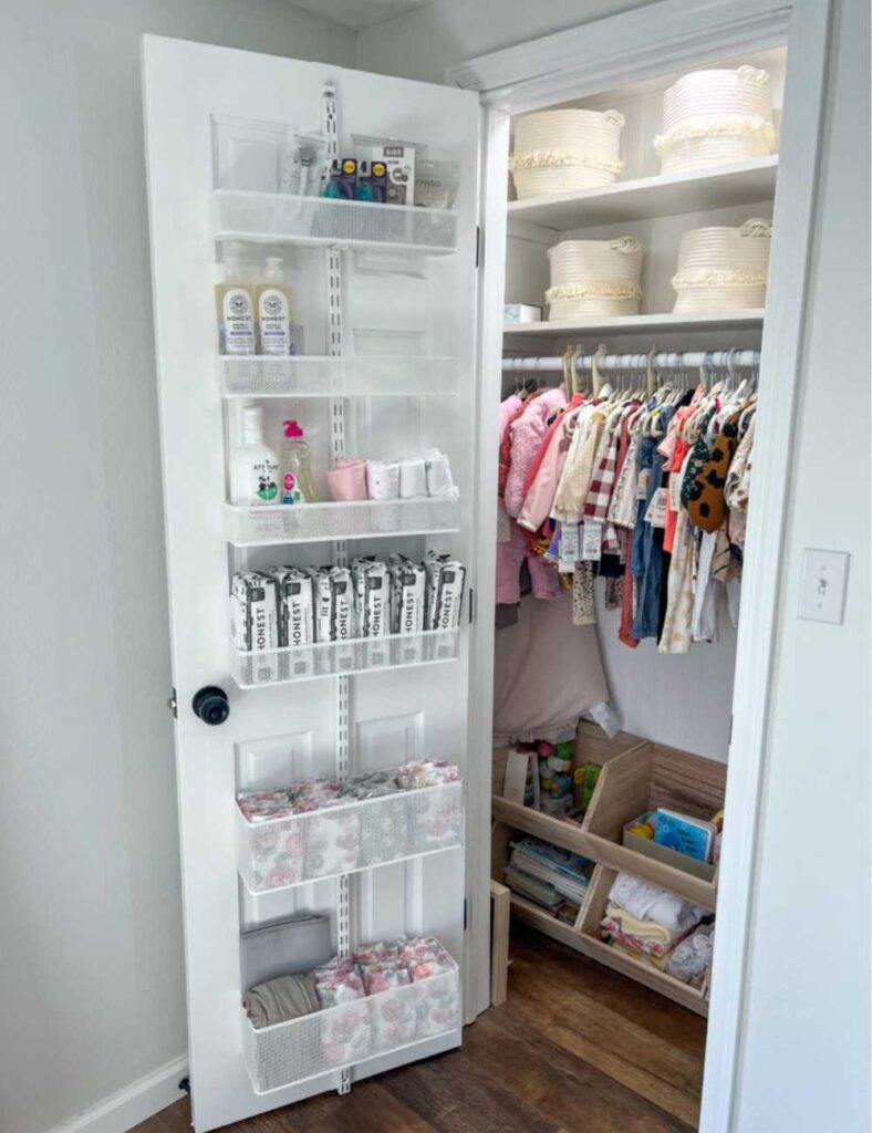 picture of a nursery closet with door opened showing an organizer hanging on the door and shelving and clothing rod in the closet.
