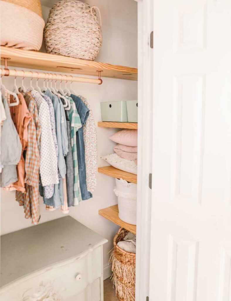 picture of a nursery closet with a clothing rod going across at the top with a shelf for storage. To the right are 3 shelves tucked into the empty space between the two walls.