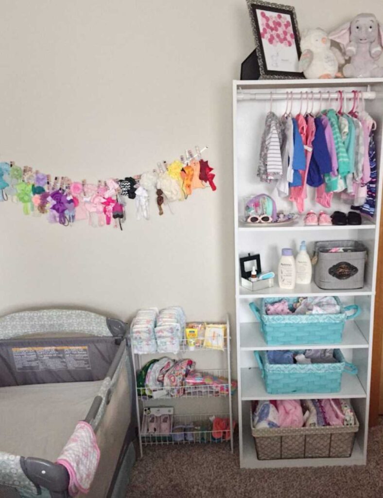 nursery with a pack n play, wire storage rack with baby essentials, and a book case converted to a closet for baby's items.