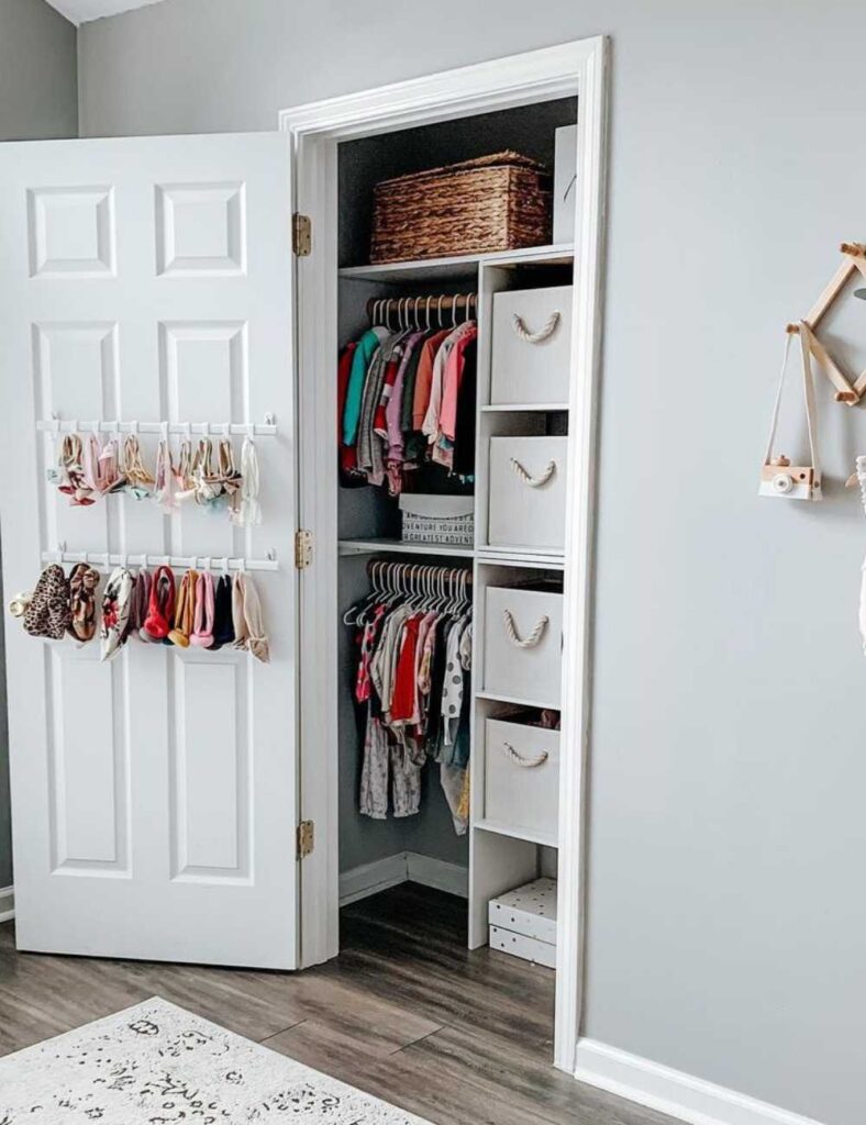 picture of a baby's nursery closet with the door open showing a rod hanging on the door to hang up bows and storage for clothing in the closet.