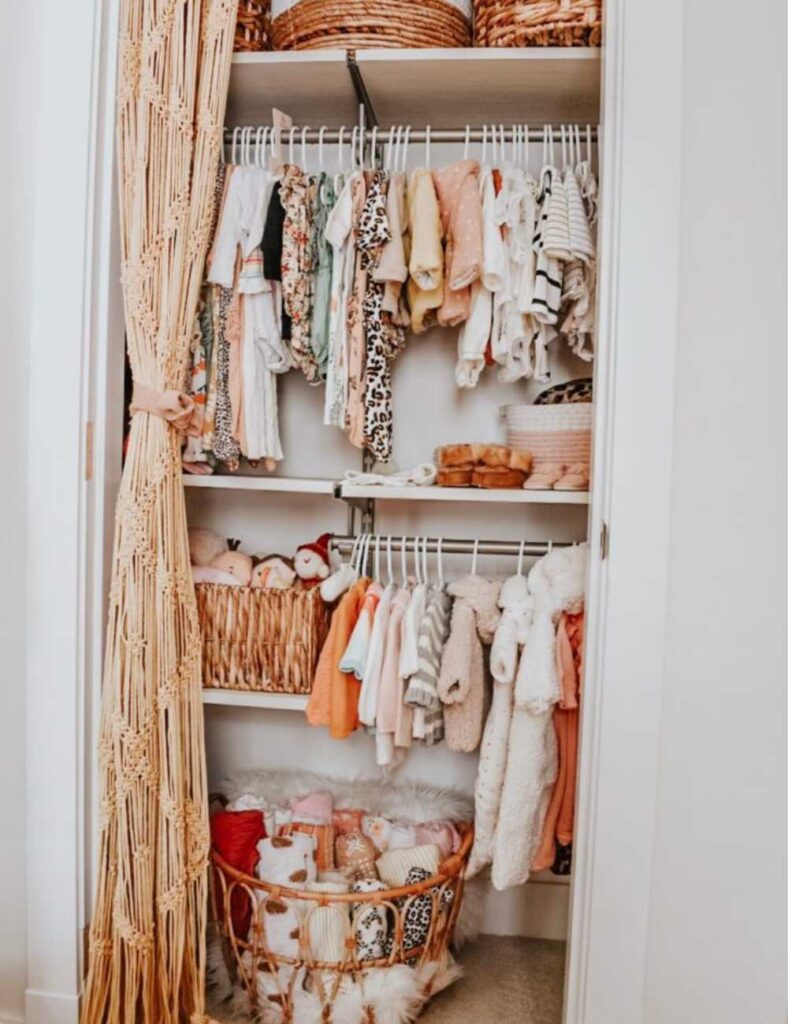 nursery closet with a curtain tied back for a door. Closet has a shelf at the top, double clothing rods, and a shelf towards the bottom. Closet is filled with baby clothing and essentials