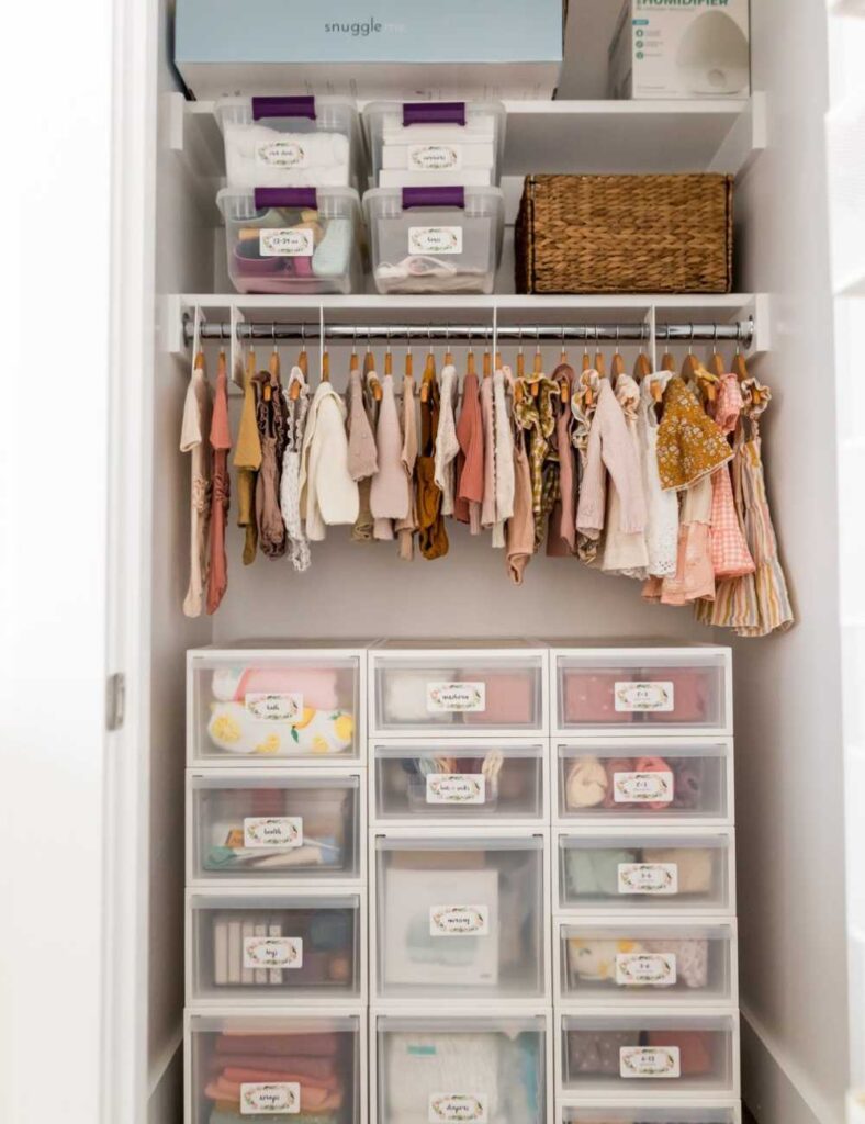 picture of nursery closet with a large plastic drawer set and a clothing rod with several outfits hanging on a shelf at the top.