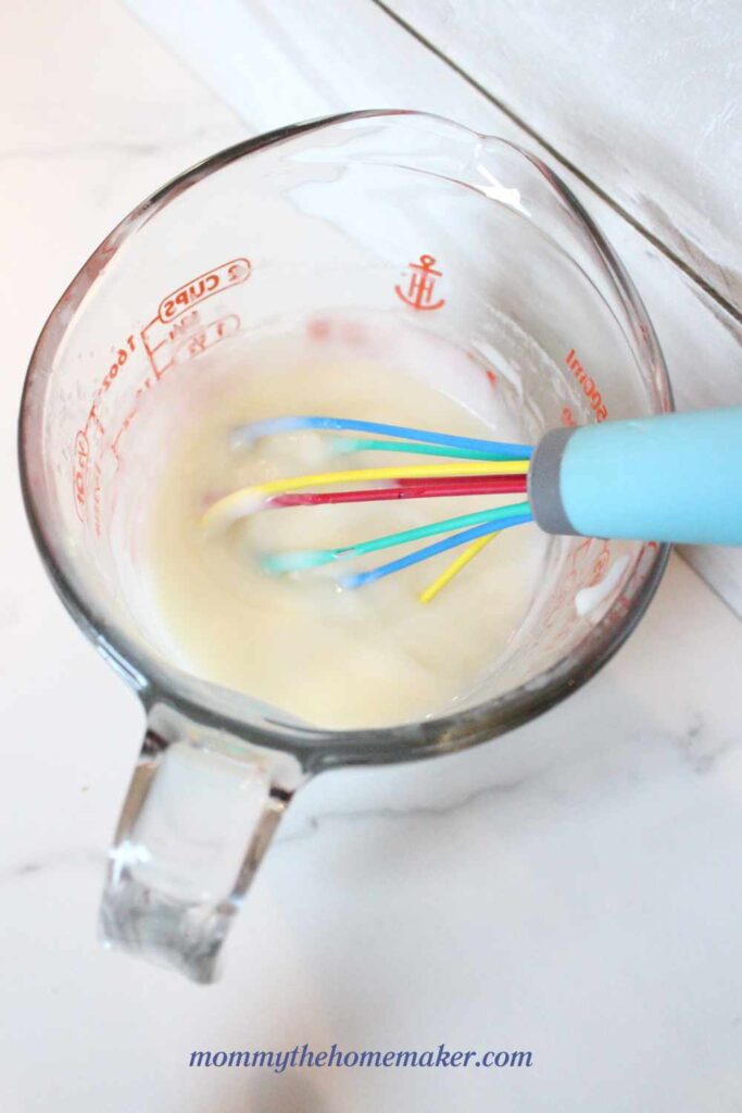 glass measuring cup with breastmilk lotion and a whisk in it