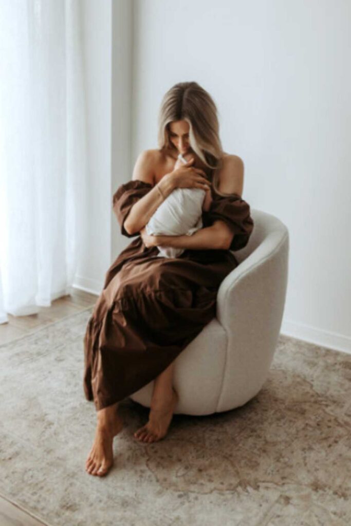 mom in brown dress holding baby in white blanket rocking him