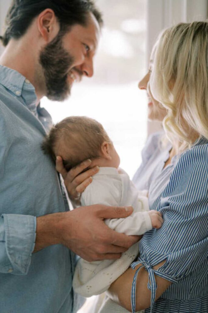 husband and wife looking at each other holding newborn baby between them