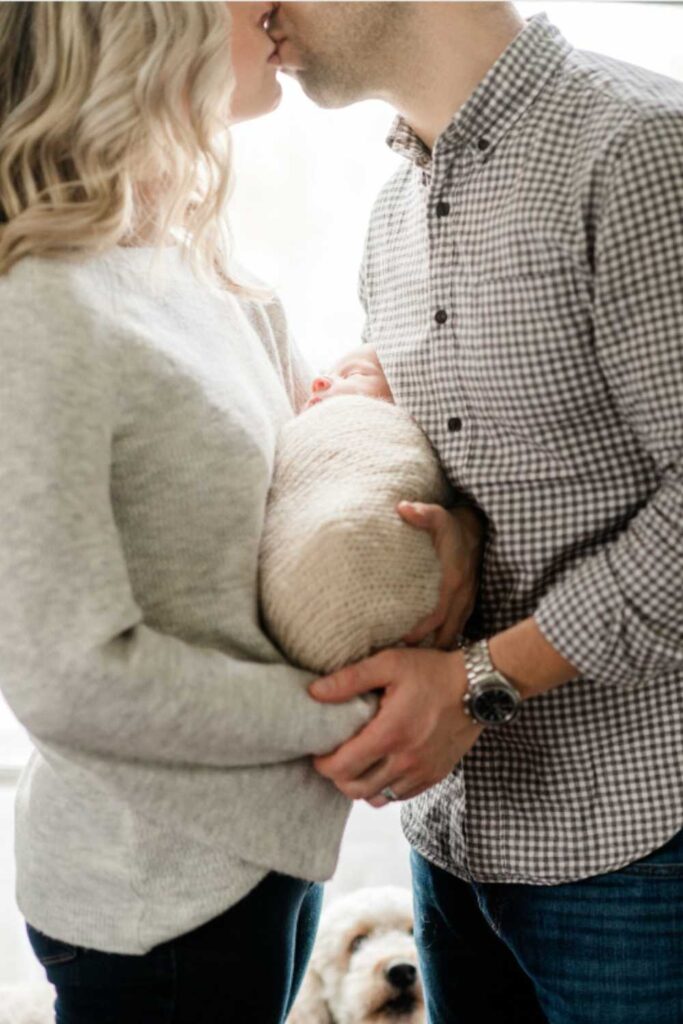 closeup of wife and husband kissing while holding newborn baby between them